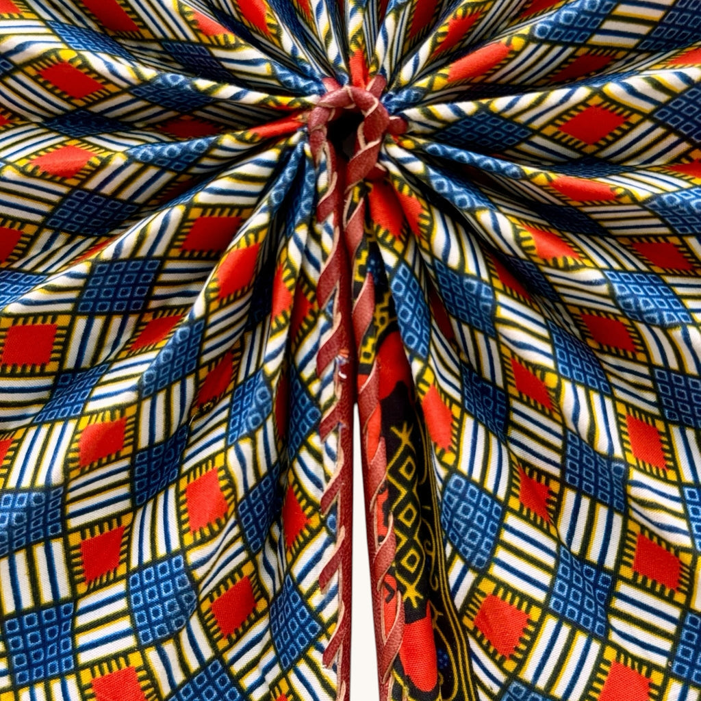 Hues by Kui handheld folding fan featuring vibrant red, blue, and white geometric Ankara print with leather handle.