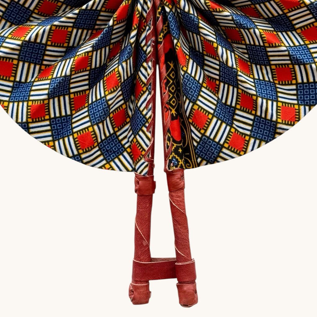 Hues by Kui handcrafted folding fan featuring vibrant red, blue, and white geometric Ankara print with leather handle.