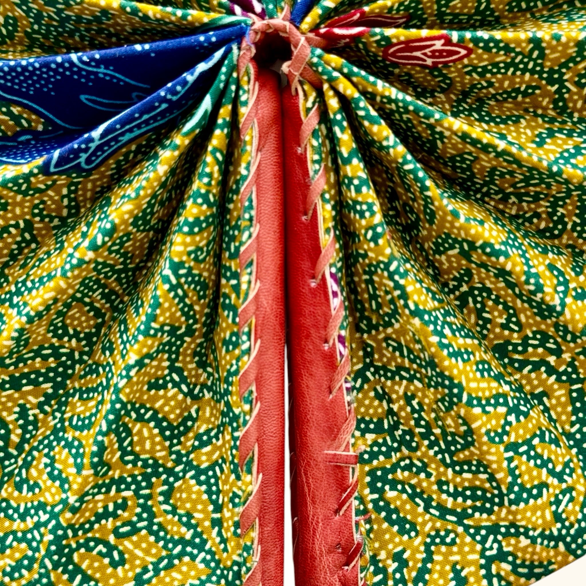 Hues by Kui handheld folding fan featuring vibrant yellow, green, and blue batik fabric with stitched leather handles.