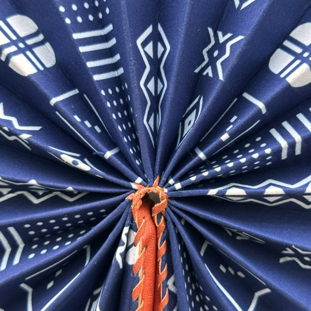 Hues by Kui handheld folding fan in deep blue fabric with white geometric mud cloth patterns and brown leather trim.