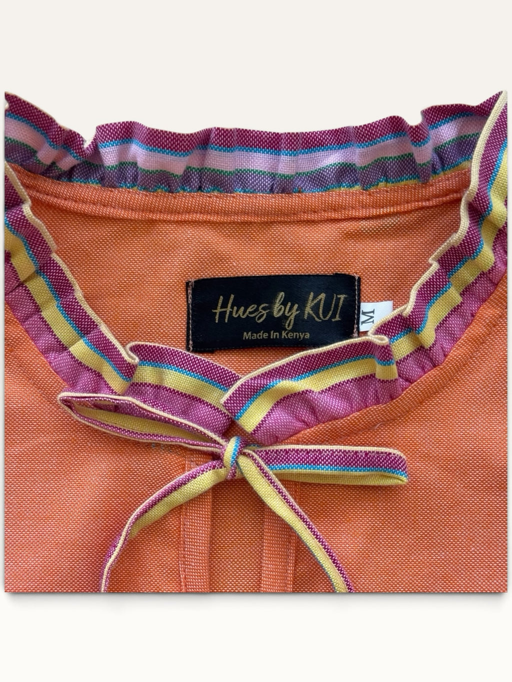Hues by Kui coral midi dress with a ruffled neckline, tie-neck detail, and colourful multi-striped trim accents.