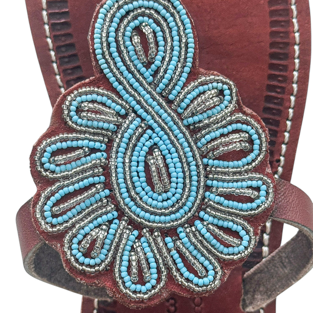 Close up of turquoise and silver hand beaded design on brown leather sandal