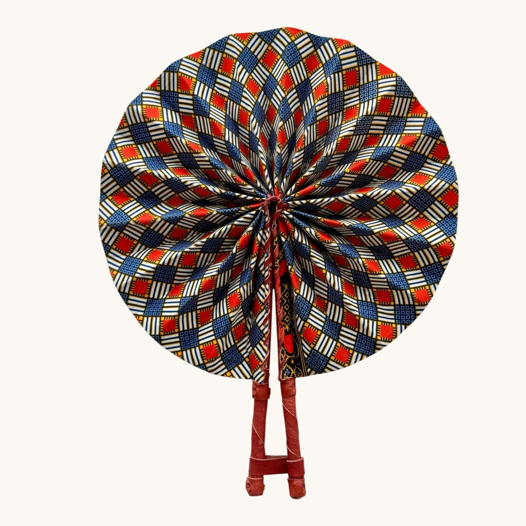 Hues by Kui traditional folding fan with vibrant red, blue, and white geometric Ankara print and leather handles.