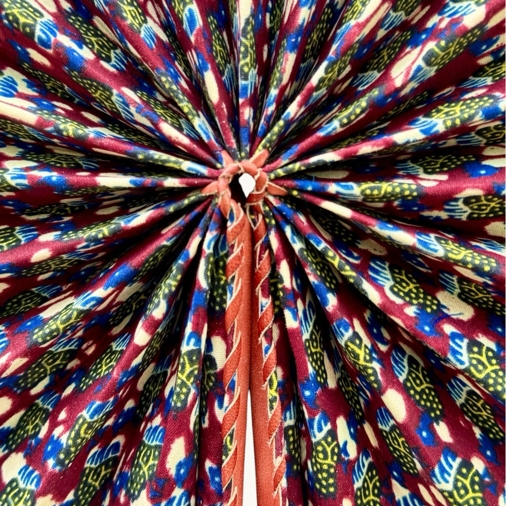 Hues by Kui handcrafted folding fan featuring vibrant African-inspired fabric in red, blue, and yellow with leather trim