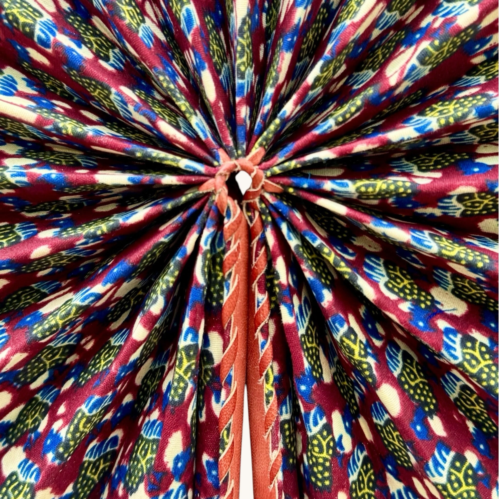 Hues by Kui handcrafted folding fan featuring vibrant African-inspired fabric in red, blue, and yellow with leather trim