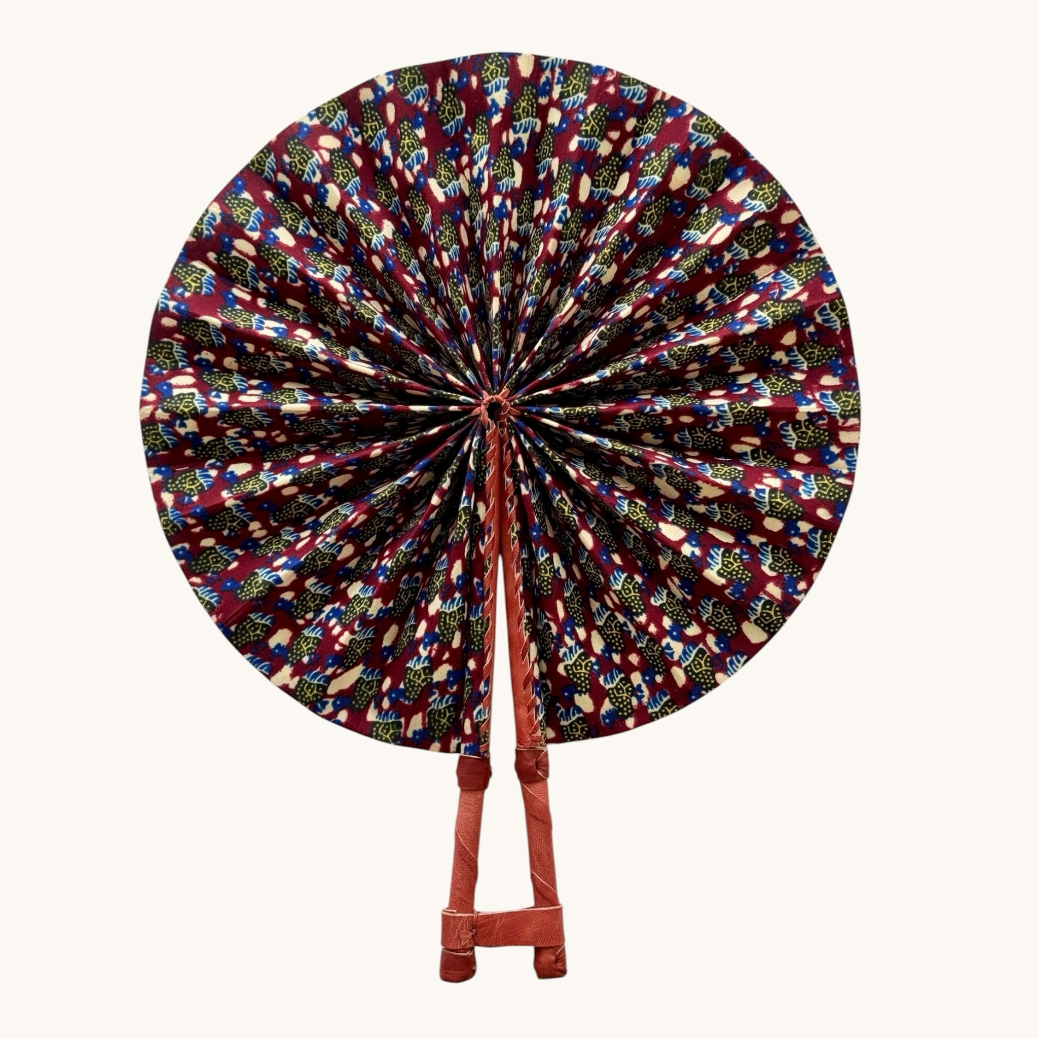 Hues by Kui handcrafted folding fan featuring vibrant African-inspired fabric in red, blue, and yellow with leather handle