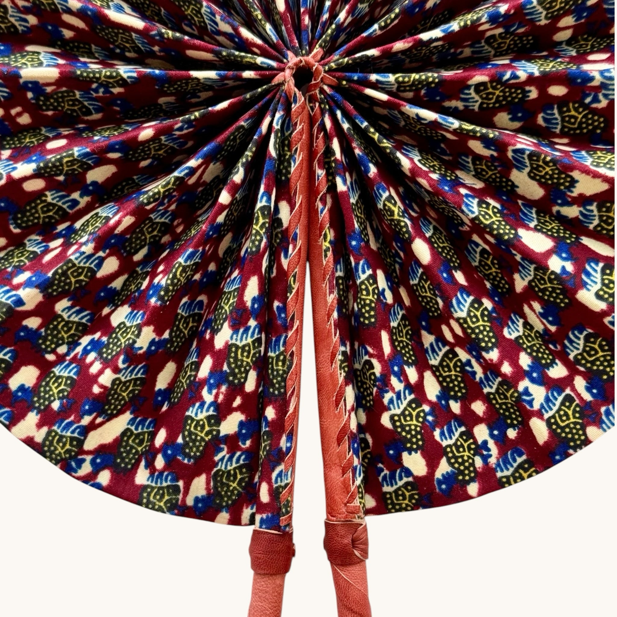 Hues by Kui handcrafted folding fan featuring vibrant red, blue, and yellow African-inspired print with leather handle.