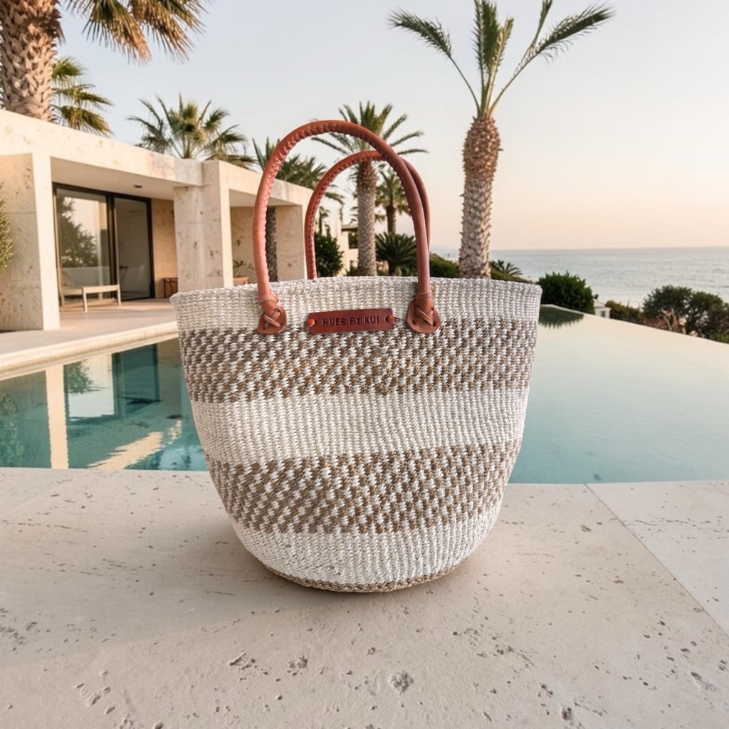 Hues by Kui handwoven tote bag with neutral striped pattern, natural fibres, and tan leather handles by a pool.