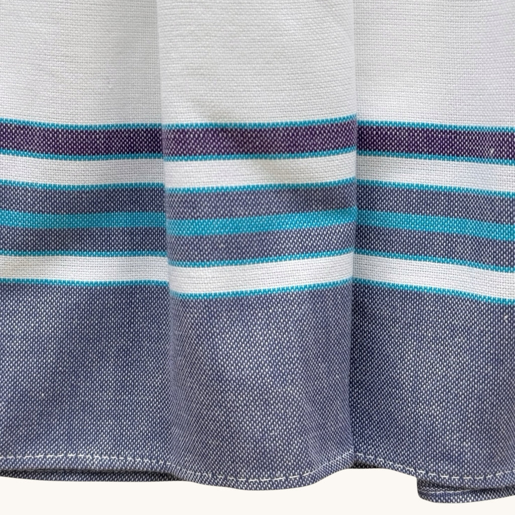 Close-up of the Hues by Kui midi dress hem featuring white fabric with horizontal blue and teal striped detailing.