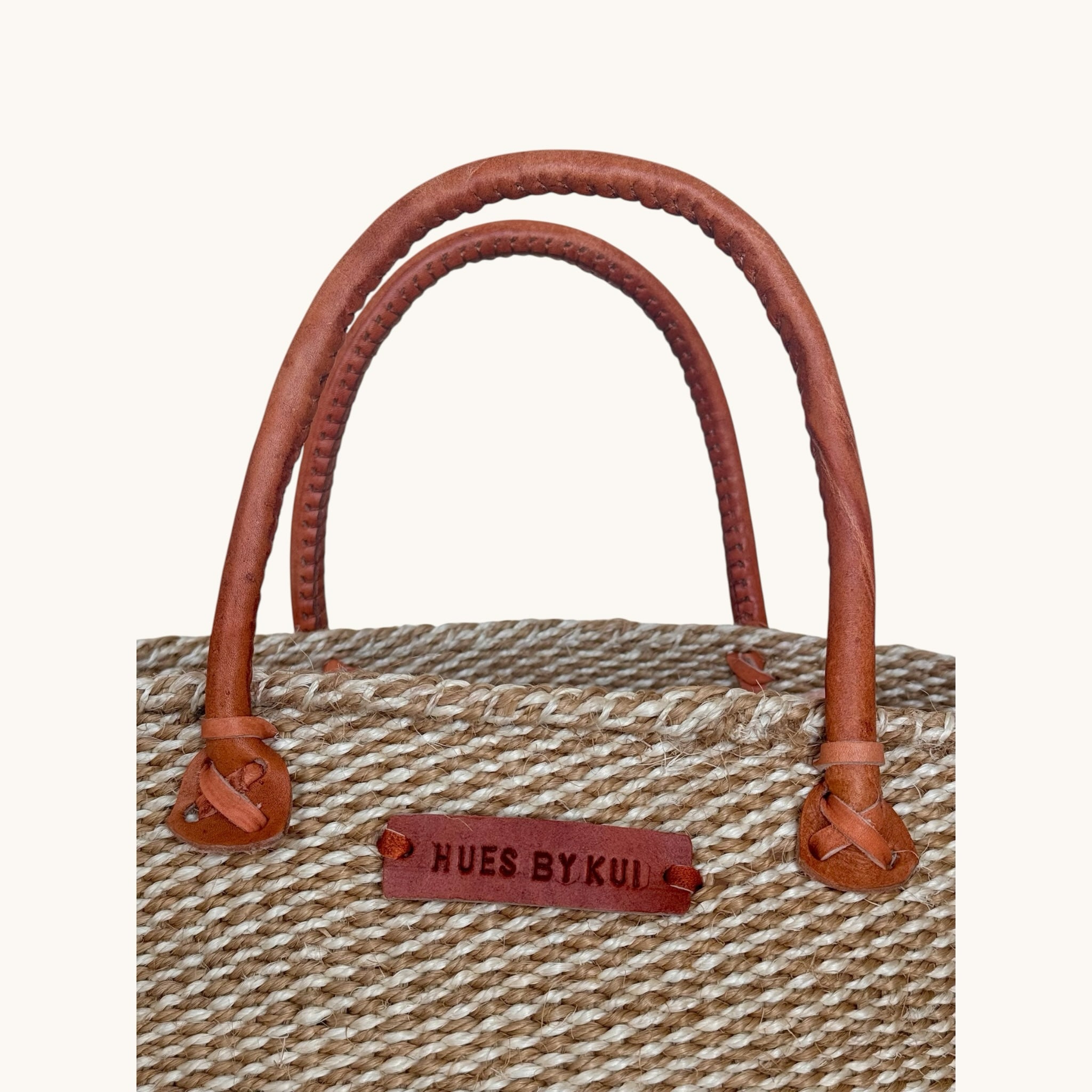 Hues by Kui handwoven natural fibre tote bag with brown leather handles and a branded leather patch detail.